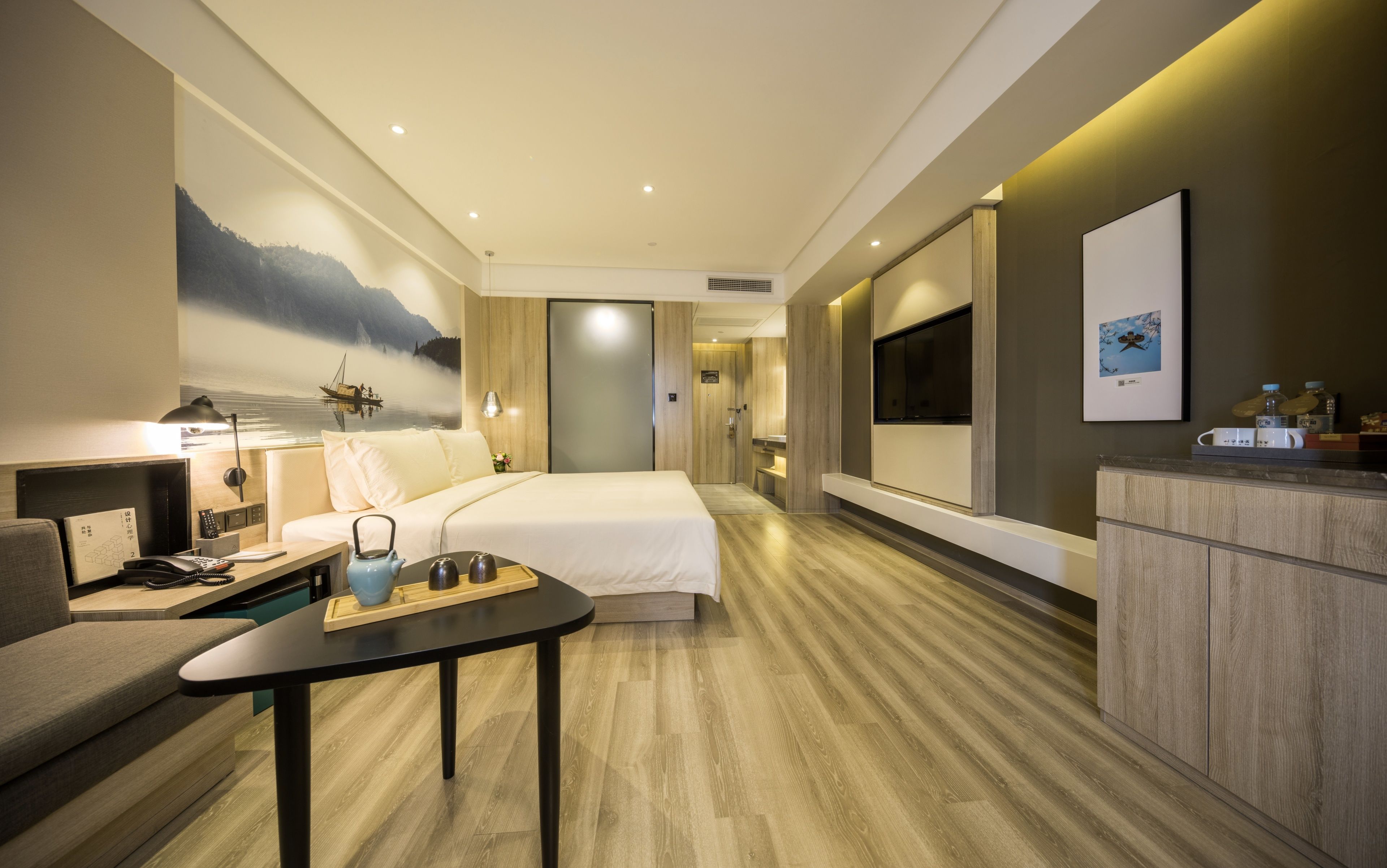 A modern hotel room with a bed, a desk, a sofa, a TV, and a painting on the wall.