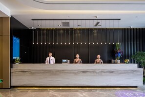 A modern reception desk with three staff members, a digital display, and a plant. - Atour Hotel People's Square Xiaoshan Hangzhou (Hangzhou)