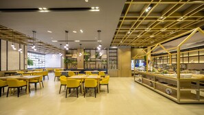 Un espace repas moderne avec des chaises et des tables jaunes, un buffet proposant divers plats et un mur décoratif agrémenté de plantes.