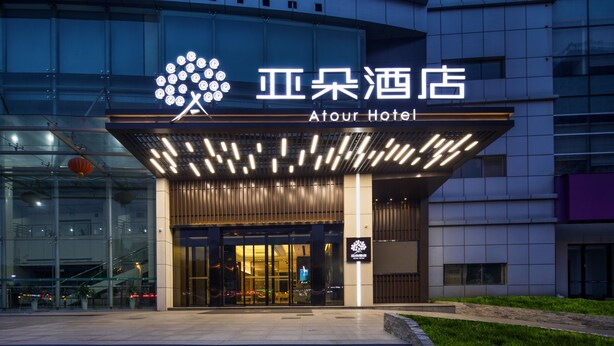 L’extérieur de l’hôtel Atour se distingue par sa façade moderne, son grand hall d’entrée vitré et son enseigne lumineuse.