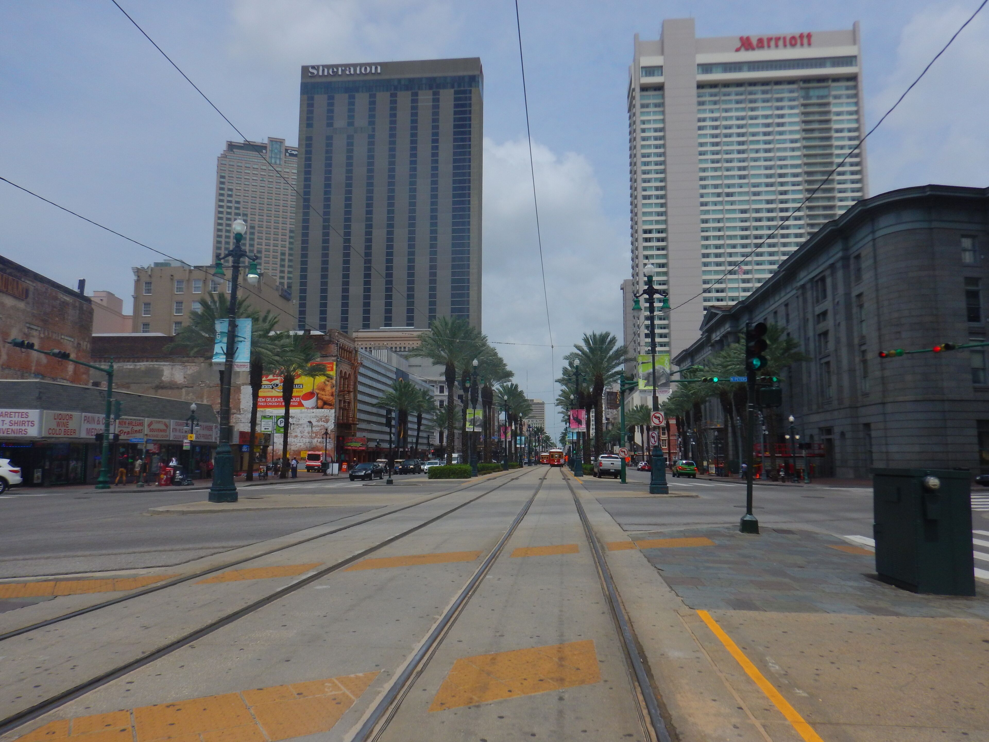 Une vue de rue avec des voies de tramway, de grands immeubles, dont les hôtels Sheraton et Marriott, et des palmiers bordant la route.