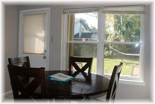 A dining area with a round table and four chairs, a window with blinds, and a view of a backyard.