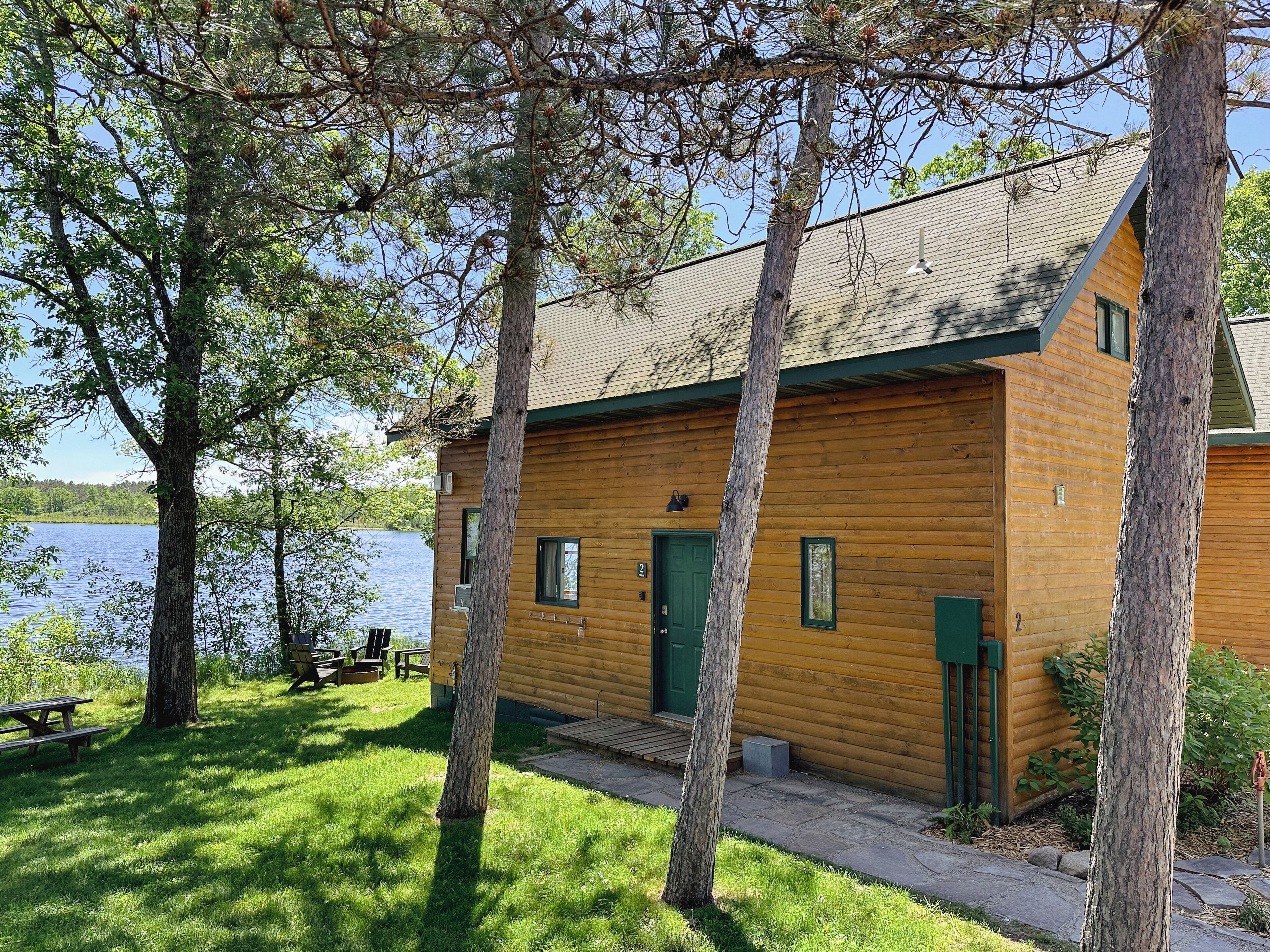A wooden cabin with a green door, a small porch, and a view of a lake.