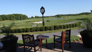 A patio with two wooden chairs and a table, overlooking a golf course with a clock post. - Coastal Greens Getaway-3 BR Golf Villa.  Plan now for a fall getaway! (Ocean View)