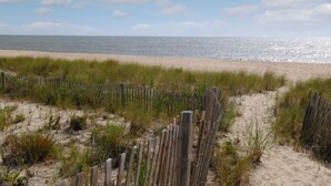 A sandy beach with a wooden fence and grass in the foreground. - Coastal Greens Getaway-3 BR Golf Villa.  Plan now for a fall getaway! (Ocean View)