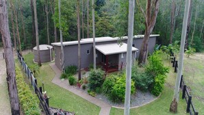 Une maison moderne à deux étages, entourée d’une forêt dense, avec une pelouse bien entretenue et une petite terrasse.