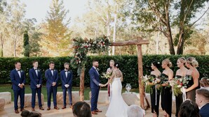 Une cérémonie de mariage en plein air, avec une arche fleurie et des invités vêtus de tenues de soirée.