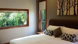 Une chambre avec une grande fenêtre, un lit agrémenté d’oreillers à motifs et une œuvre d’art représentant des arbres, accrochée au mur.