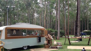 Une caravane ancienne aménagée avec un coin repas installé dans un espace boisé.