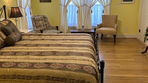 A bedroom with a large bed, two chairs, a ceiling fan, and a window with curtains. - Kaiser House in the heart of the Texas Hill Country (Harper)