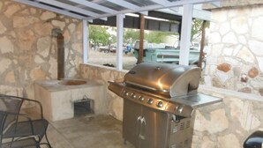 An outdoor patio with a stone wall, a stainless steel grill, and a seating area with metal chairs. - Kaiser House in the heart of the Texas Hill Country (Harper)