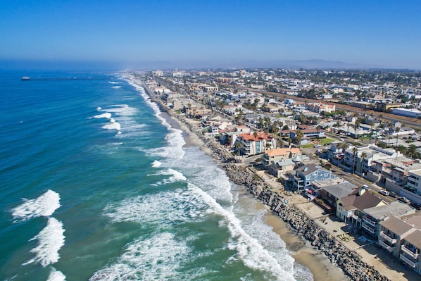 An aerial view of a coastal town with a beach, buildings, and a pier.