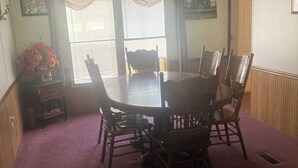 Uma sala de jantar com uma mesa redonda e seis cadeiras, um candelabro e uma janela com persianas.