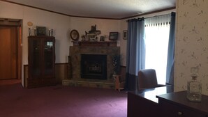 Uma sala de estar com lareira, um armário de madeira, uma poltrona e uma escrivaninha.