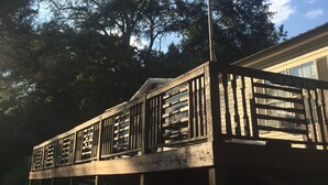 Um deck de madeira com uma bandeira americana, rodeado por árvores e uma casa ao fundo.