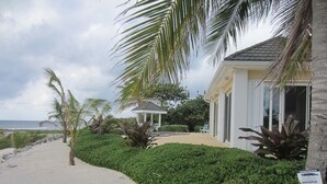 A beachfront property with a sandy path leading to a building with a white exterior and large windows. - Secluded Waterfront Single Family Villa with Private Pool – 3,000 Sq of Luxury (East End - Half Moon Bay)