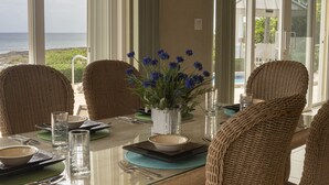 A dining table set with wicker chairs, a vase of blue flowers, and a view of the ocean. - Secluded Waterfront Single Family Villa with Private Pool – 3,000 Sq of Luxury (East End - Half Moon Bay)