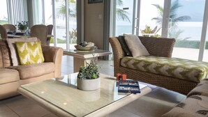 A spacious living area with a glass coffee table, wicker furniture, and a view of the ocean. - Secluded Waterfront Single Family Villa with Private Pool – 3,000 Sq of Luxury (East End - Half Moon Bay)