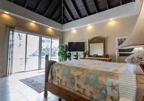 A bedroom with a large bed, a TV, a mirror, and a sliding glass door leading to a balcony.