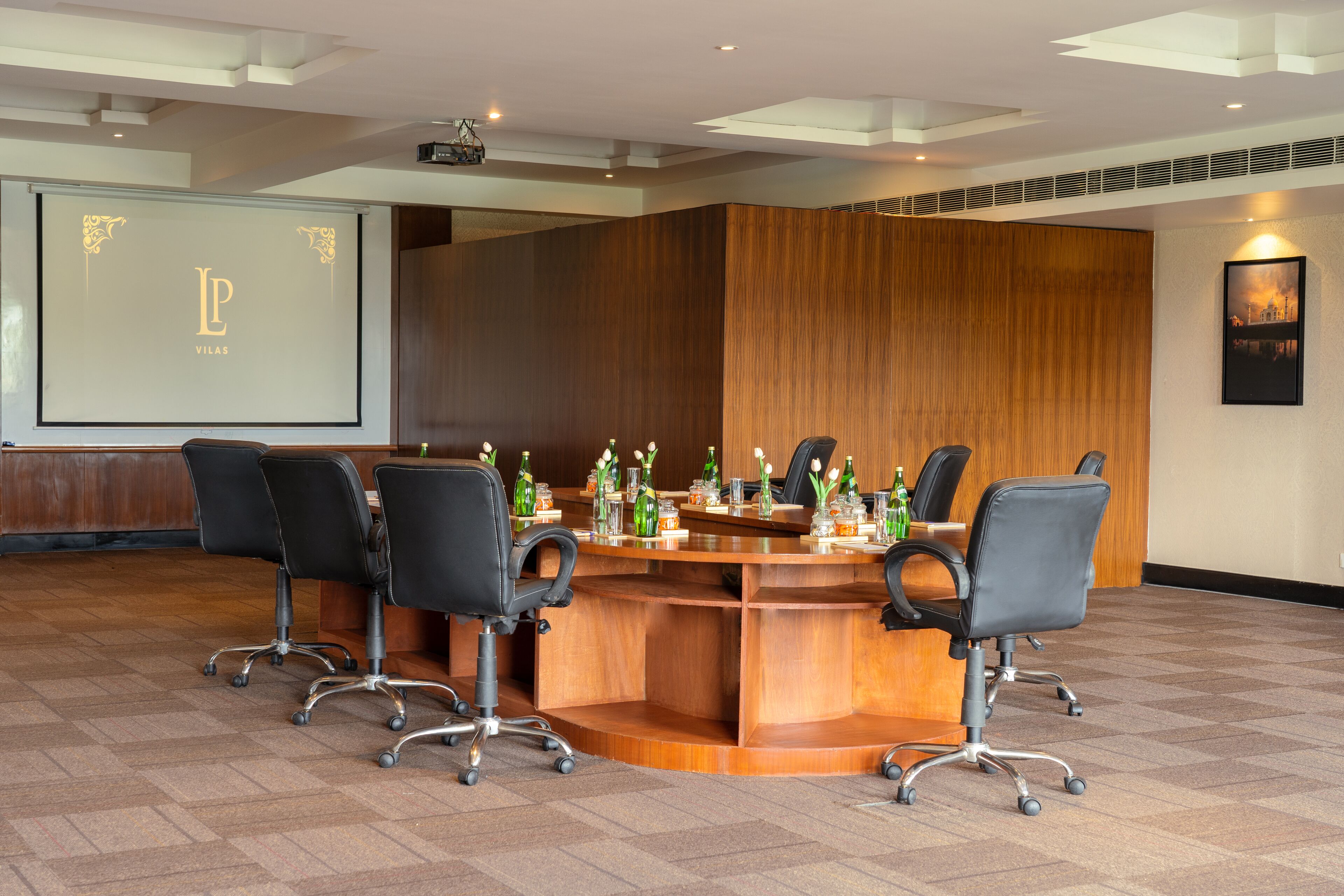 A conference room with a wooden table, black chairs, and a projector screen displaying "LP VILAS".