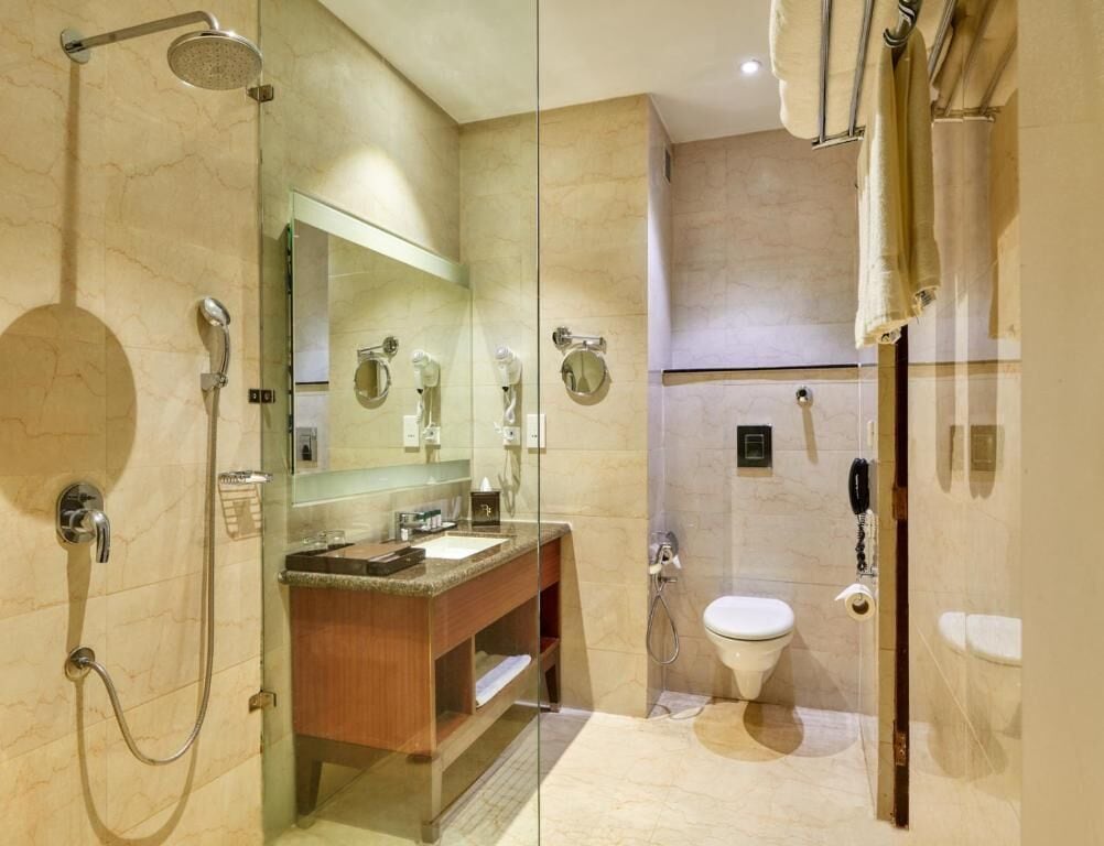 A modern bathroom with a glass-enclosed shower, a wooden vanity, a round mirror, and a toilet.