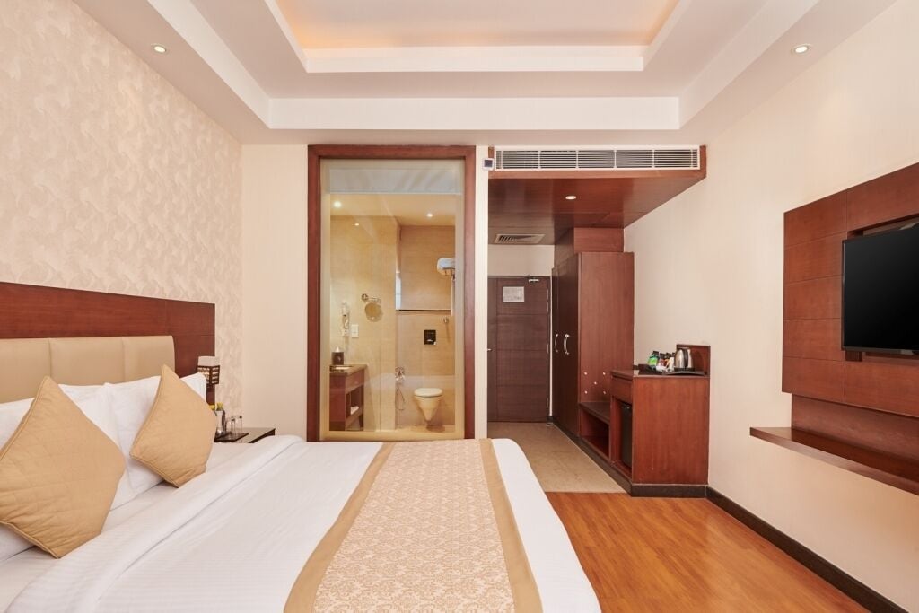 A hotel room with a large bed, a TV mounted on the wall, a separate bathroom, and a small kitchenette area.