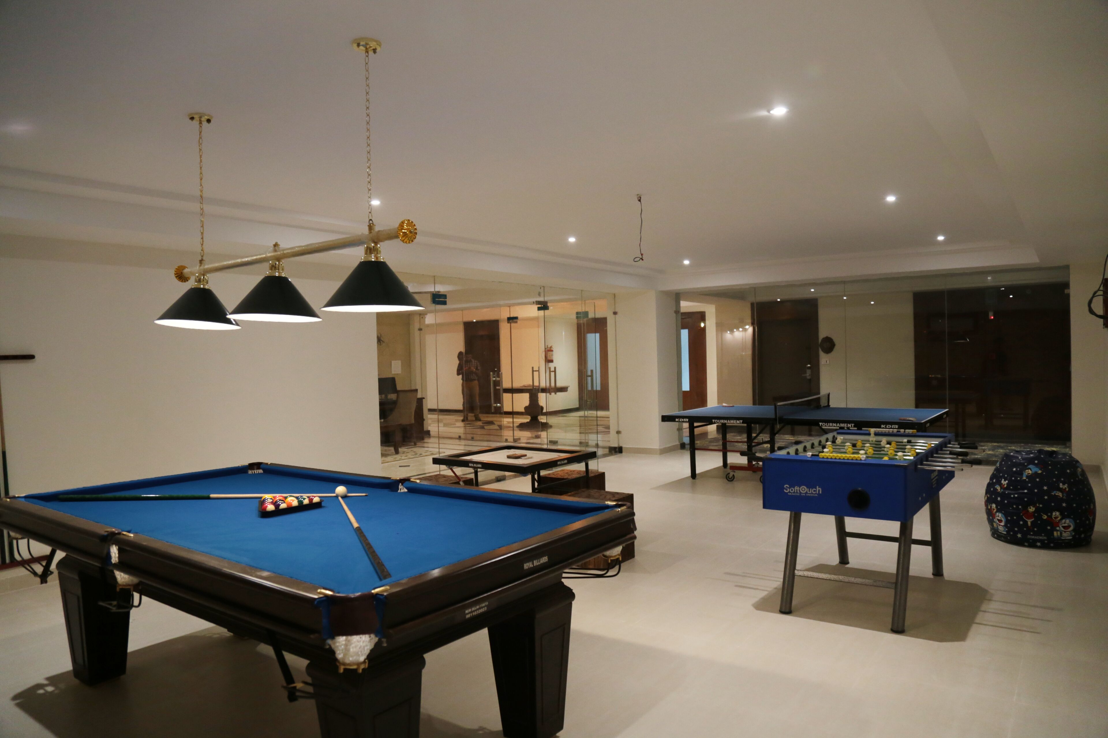 A pool table with a foosball table and a table tennis table in a room with a high ceiling and recessed lighting.