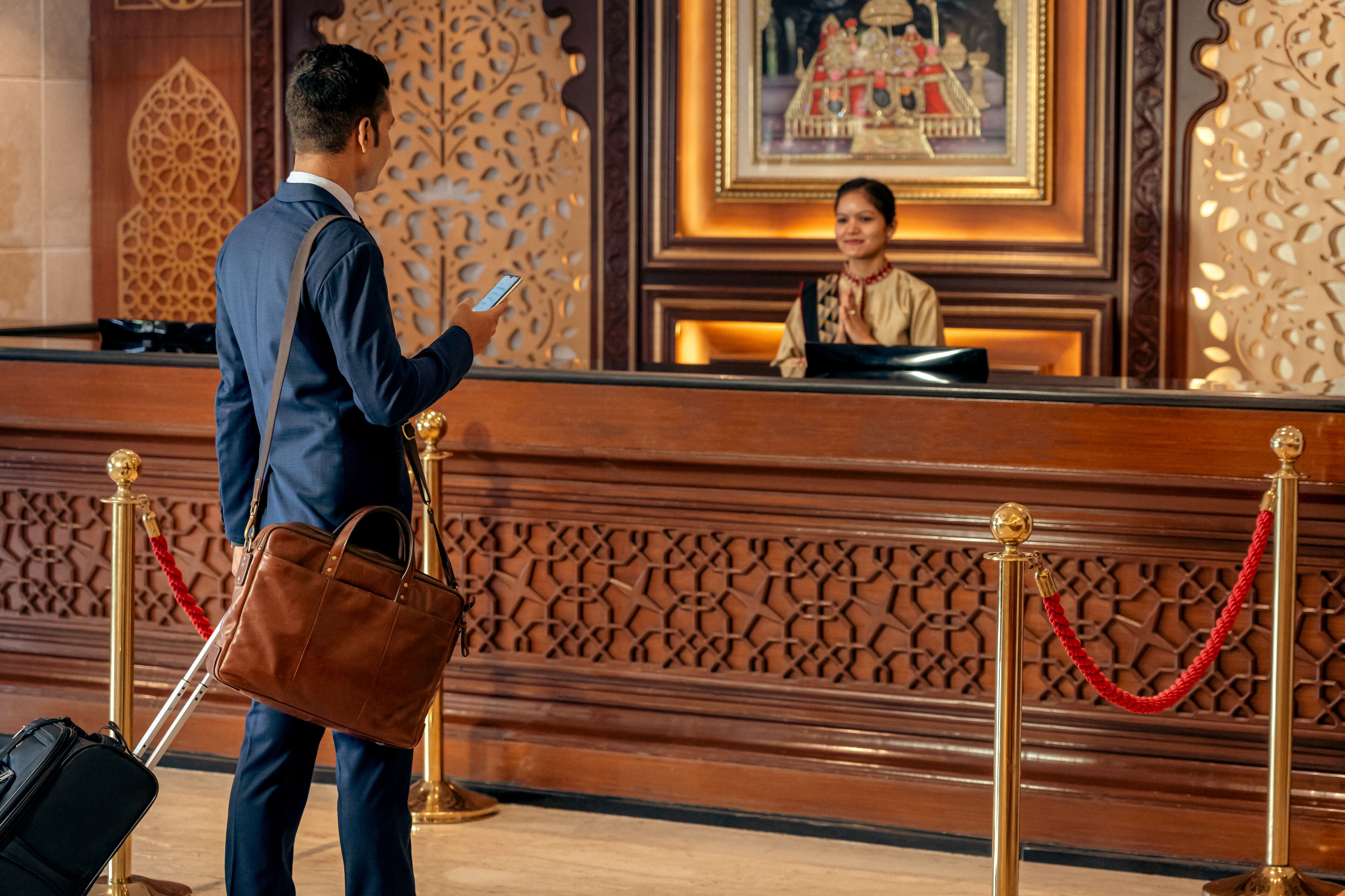 A man in a suit with a briefcase and a brown bag standing at a reception desk with a woman behind it.