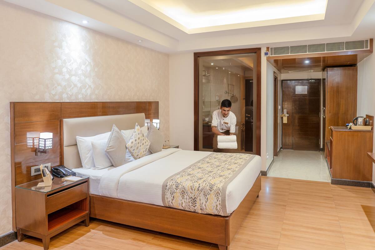 Quarto de hotel com uma cama grande, uma mesa de cabeceira de madeira, uma escrivaninha e um guarda-roupa.