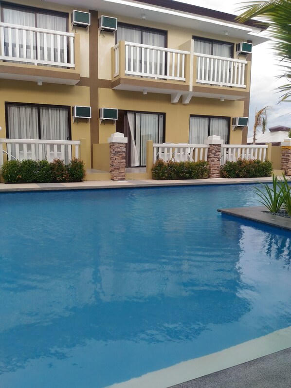 A hotel with a swimming pool, balconies with white railings, and air conditioning units. - Aquamira Hotel & Resort (Tanza)