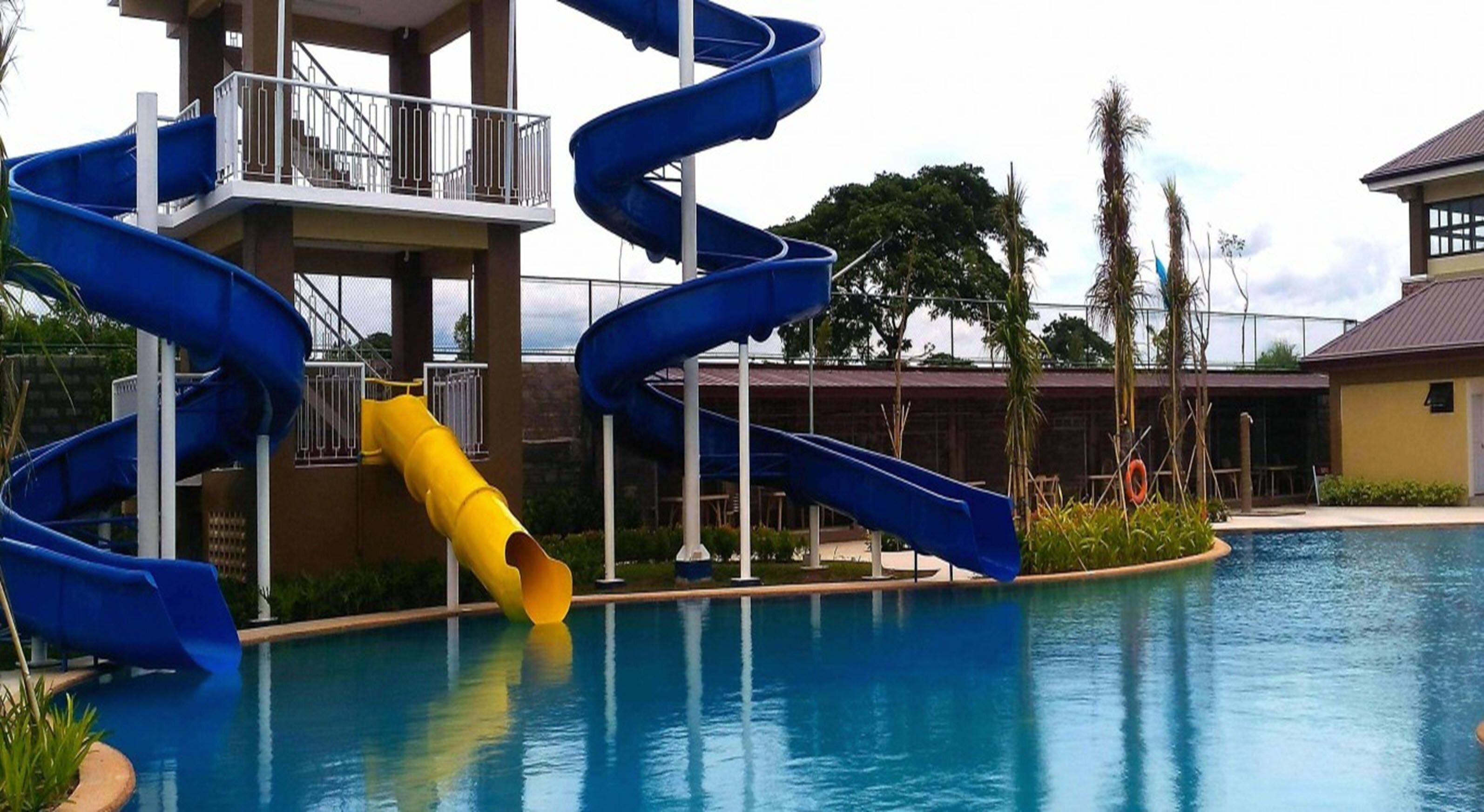 Un área de piscina con un tobogán en espiral azul y un tobogán amarillo, rodeada por un edificio con balcón.