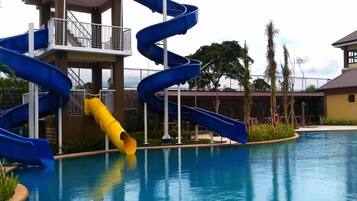 Un área de piscina con un tobogán en espiral azul y un tobogán amarillo, rodeada por un edificio con balcón.