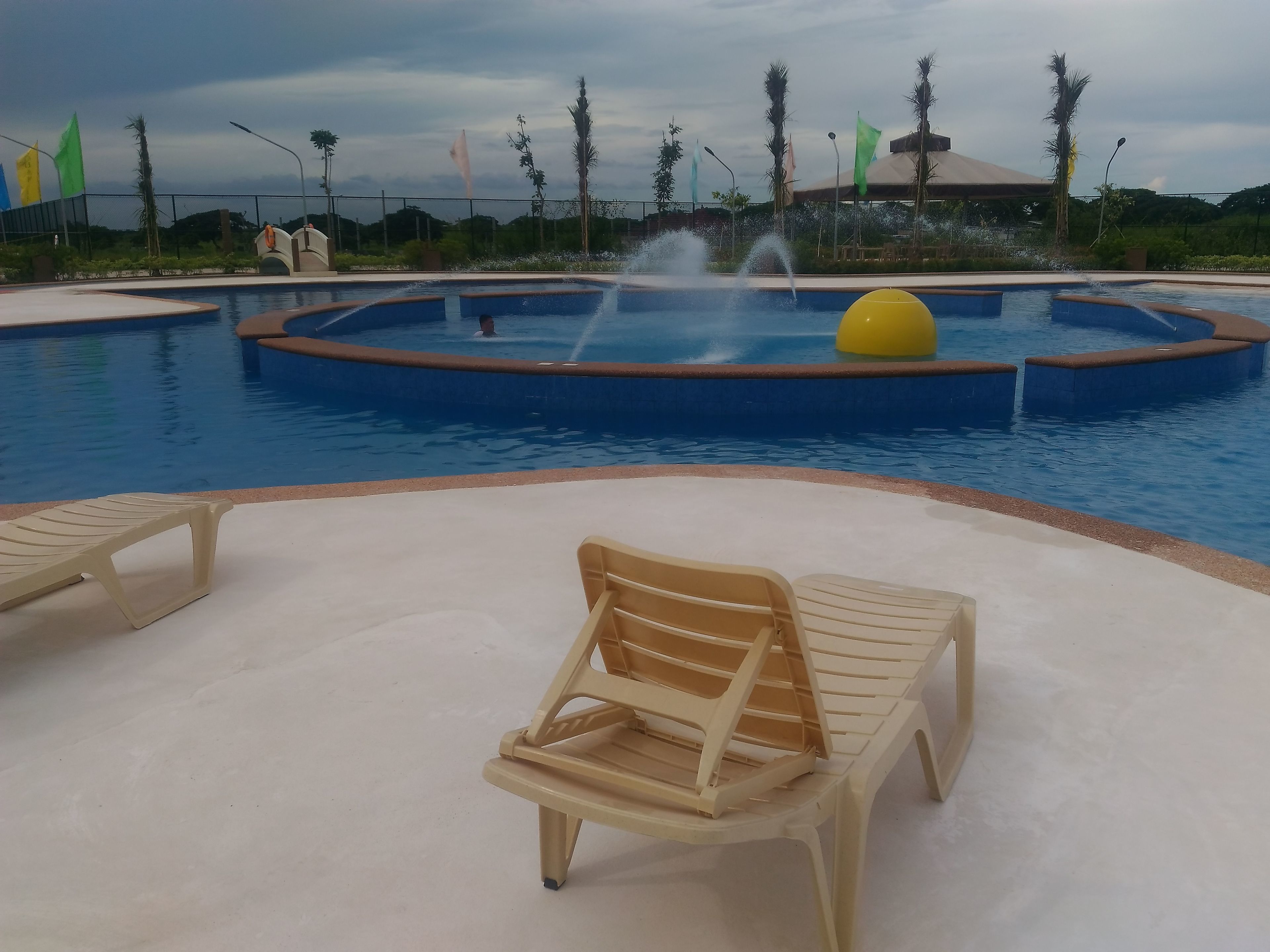 A swimming pool with a fountain, surrounded by palm trees and flags.