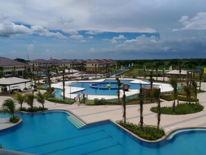 A resort with multiple swimming pools, palm trees, and a clear sky. - Aquamira Hotel & Resort (Tanza)
