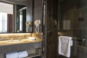 Une salle de bain moderne avec un grand miroir, un lavabo, une douchette à main et un porte-serviettes avec une serviette.