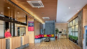 A modern hotel lobby with a wooden reception desk, seating area, and potted plants. - ibis Kunshan Changjiang Rd Hotel (Suzhou)