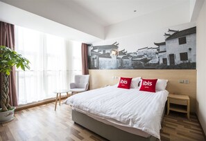 A hotel room with a large bed, a chair, a nightstand, and a wall-mounted painting of traditional buildings. - ibis Kunshan Changjiang Rd Hotel (Suzhou)