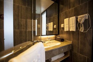 Une salle de bain moderne avec un grand miroir, des carreaux de couleur sombre, un lavabo et un porte-serviettes.
