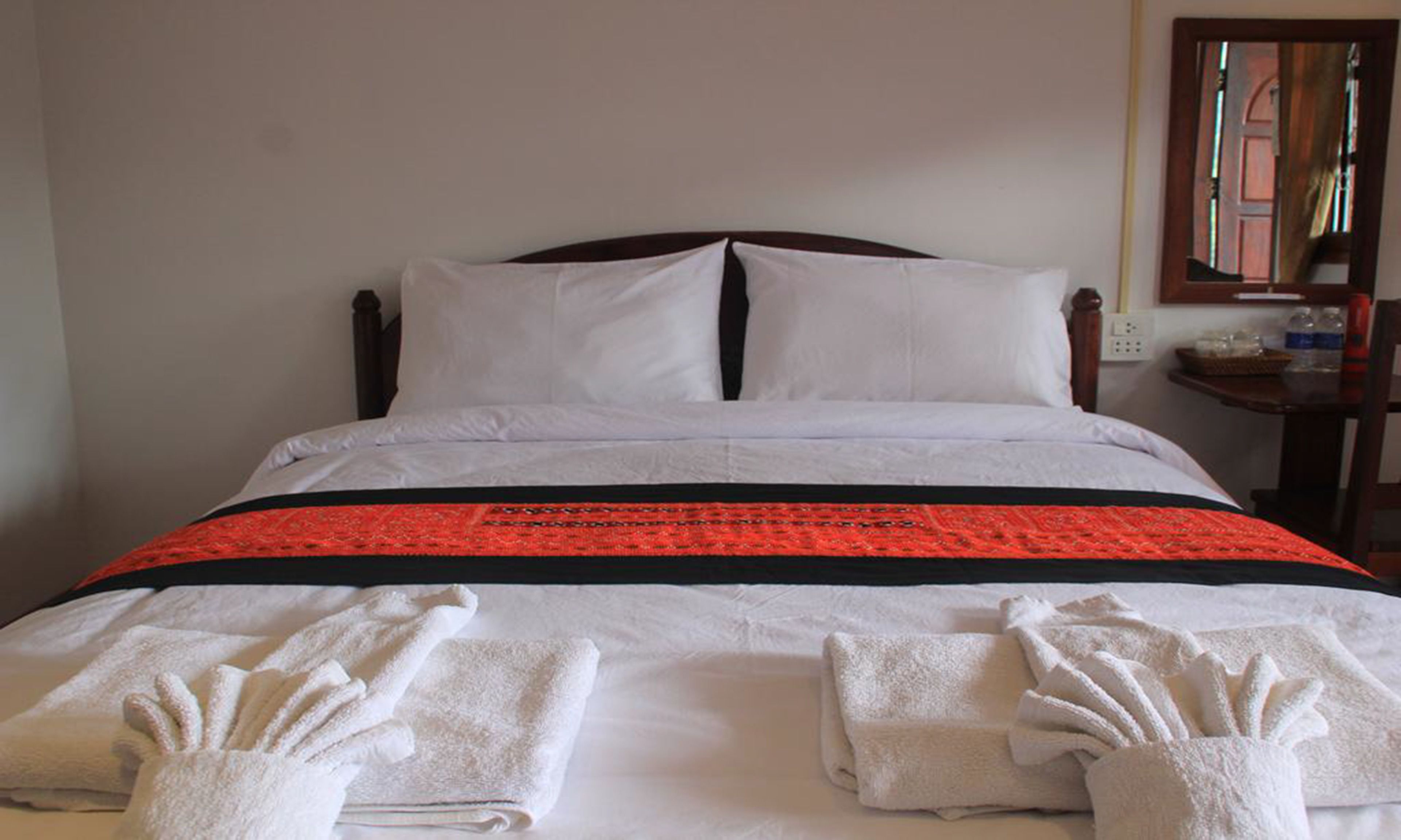Una cama bien hecha con sábanas blancas y una colcha estampada en rojo y negro.