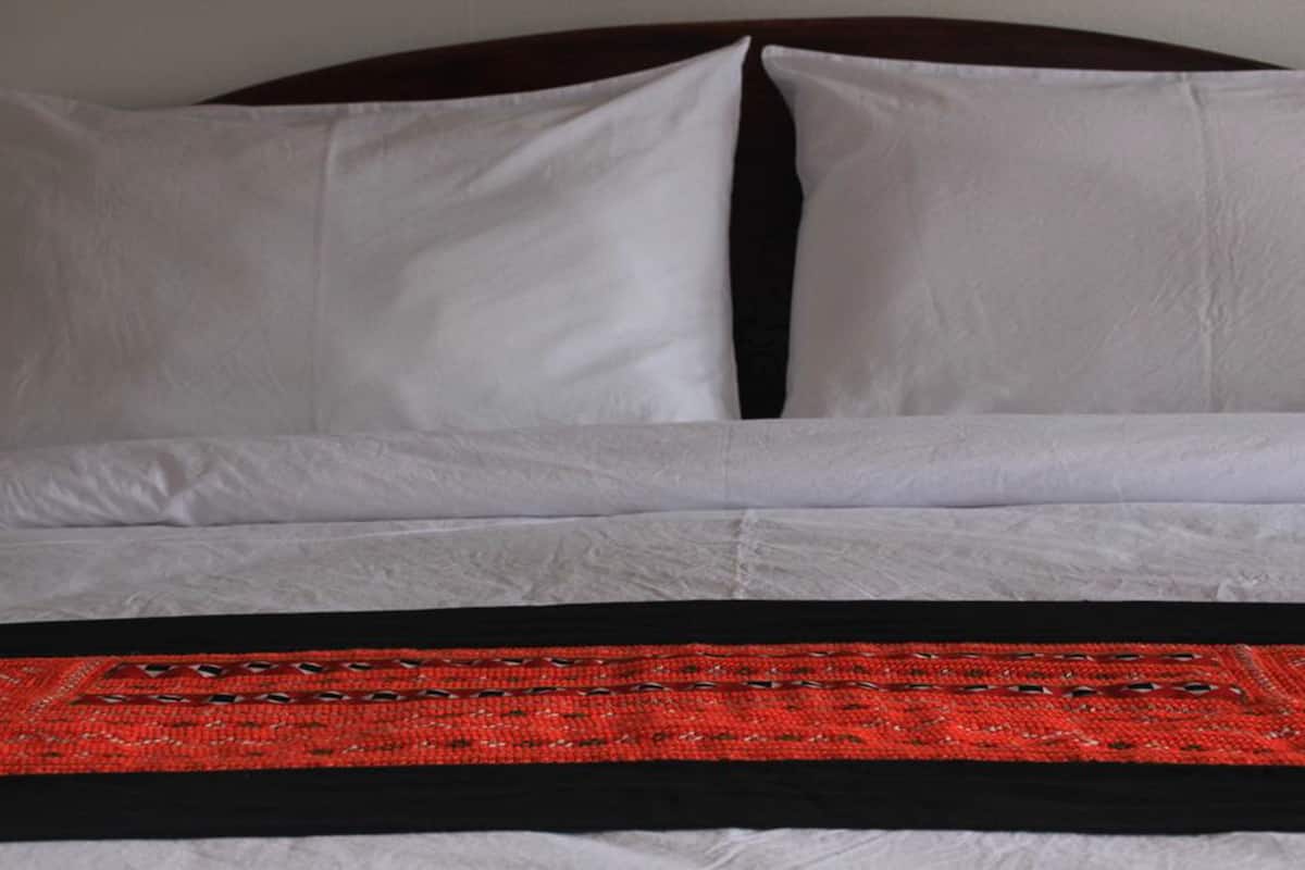 Ein Bett mit weißer Bettwäsche und einer Decke mit roten und schwarzen Mustern.