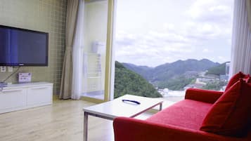 Habitación de hotel con sofá rojo, televisión montada en la pared, una mesa y vista a las montañas por la ventana.
