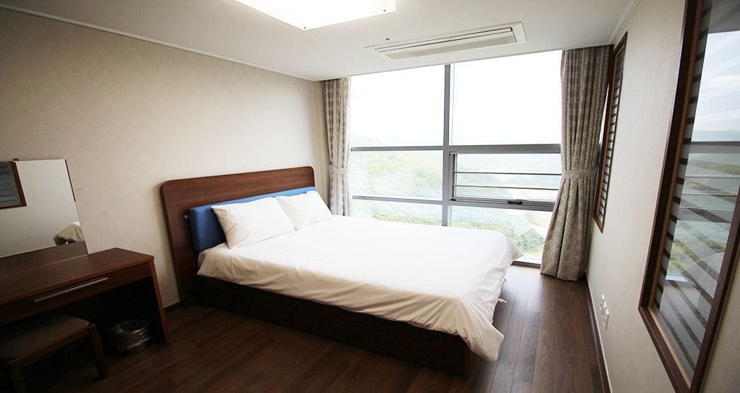 Une chambre d’hôtel équipée d’un lit, d’un bureau et d’une grande fenêtre donnant sur un paysage agréable.
