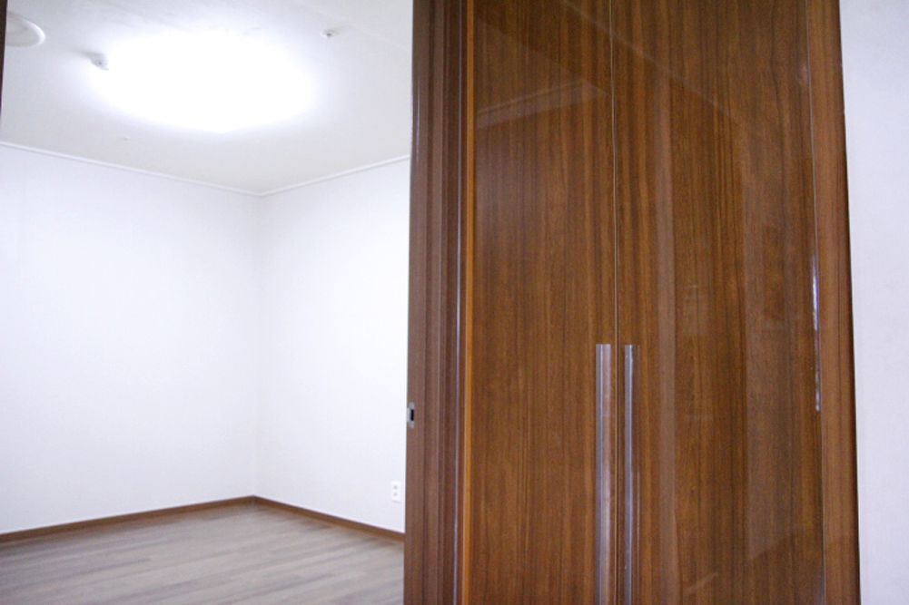 A room with a wooden wardrobe, white walls, and a wooden floor.