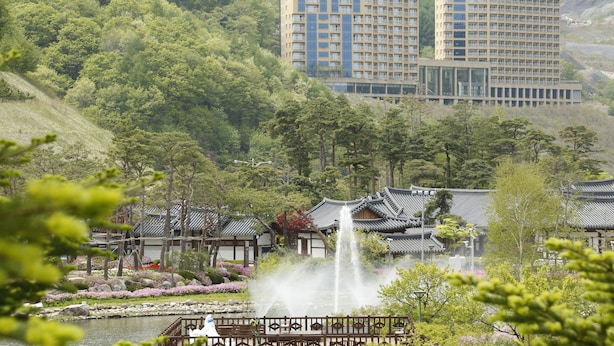 A traditional Japanese-style building with a garden, a fountain, and a view of modern high-rise buildings in the background. - High Castle Resort (Jeongseon)