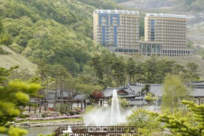 A traditional Japanese-style building with a garden, a fountain, and a view of modern high-rise buildings in the background. - High Castle Resort (Jeongseon)