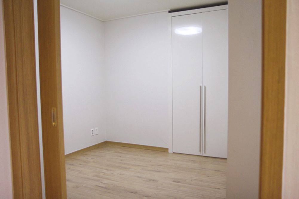 A room with a wooden floor, white walls, and a white wardrobe with two doors.