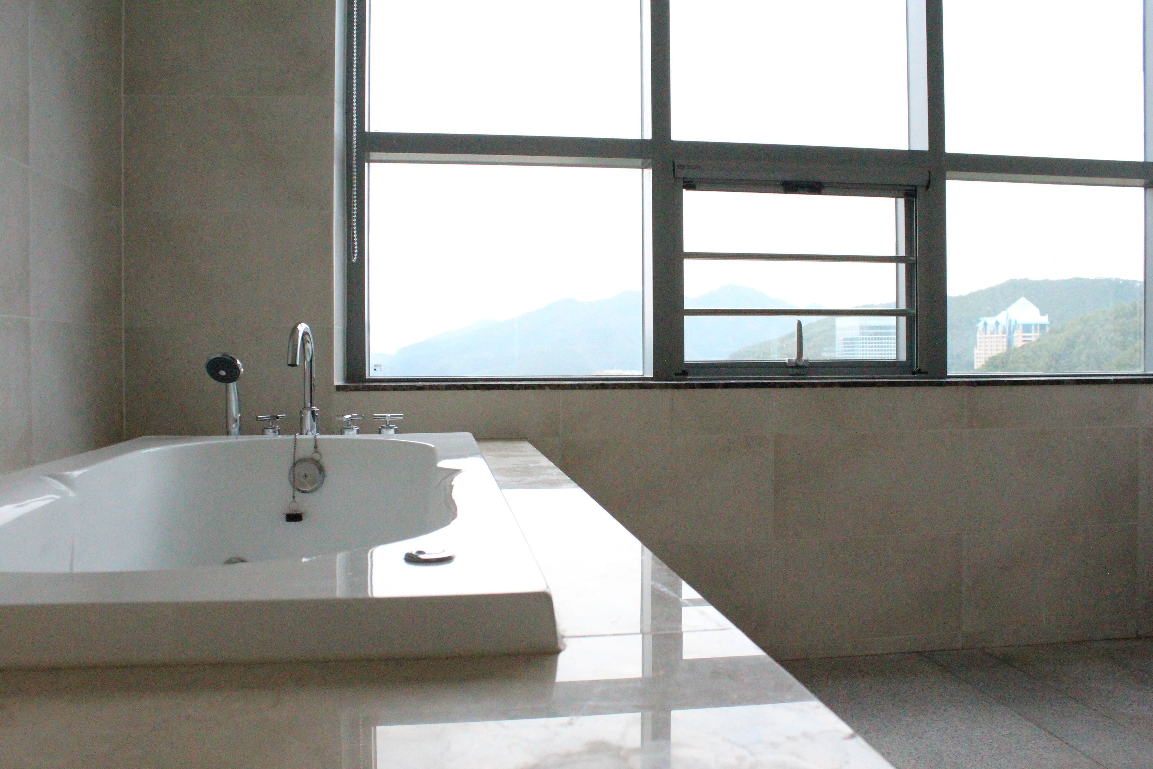 A modern bathroom with a large bathtub, a window with a view of mountains, and a tiled floor.