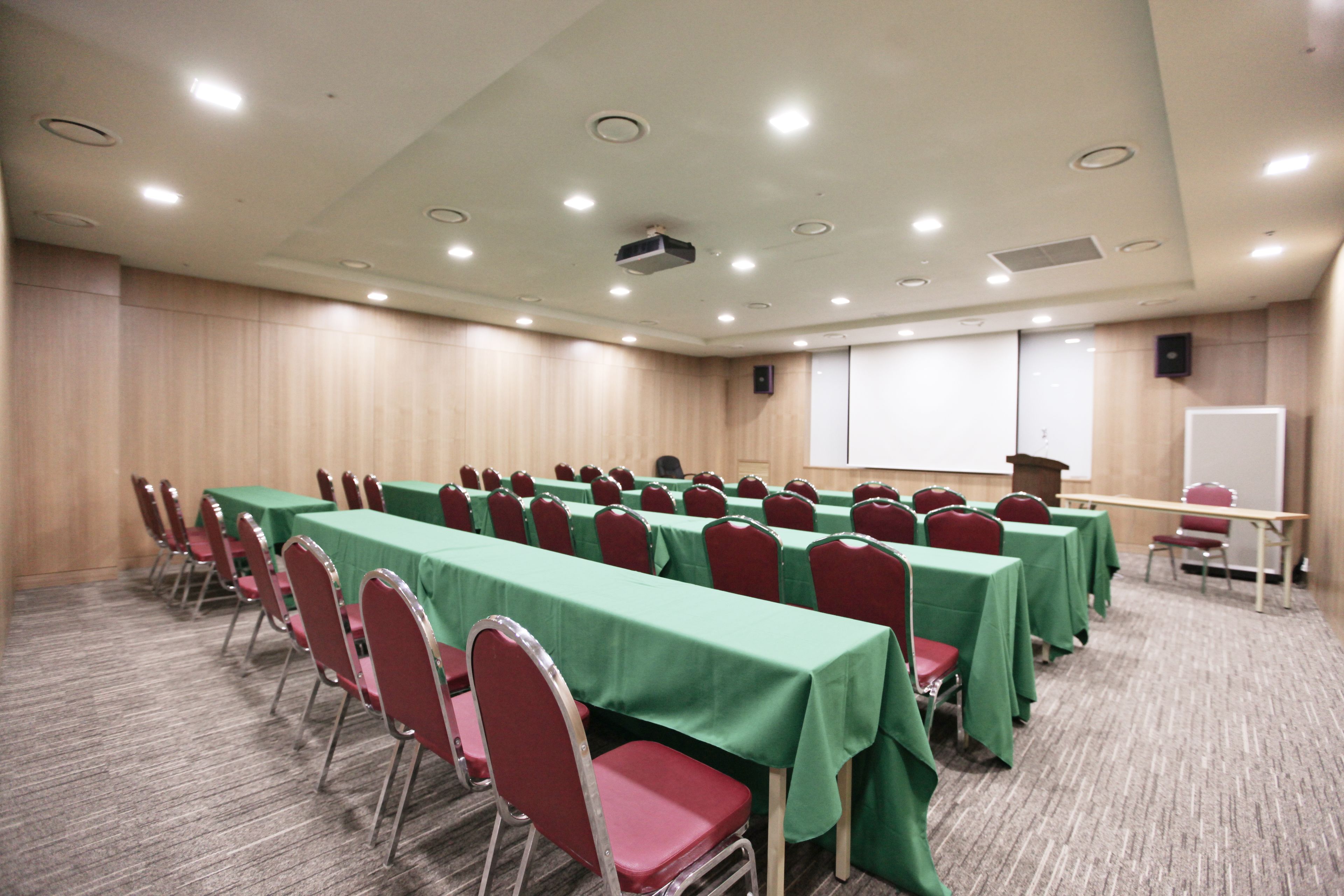 A conference room with rows of tables and chairs, a projector screen, and a whiteboard.