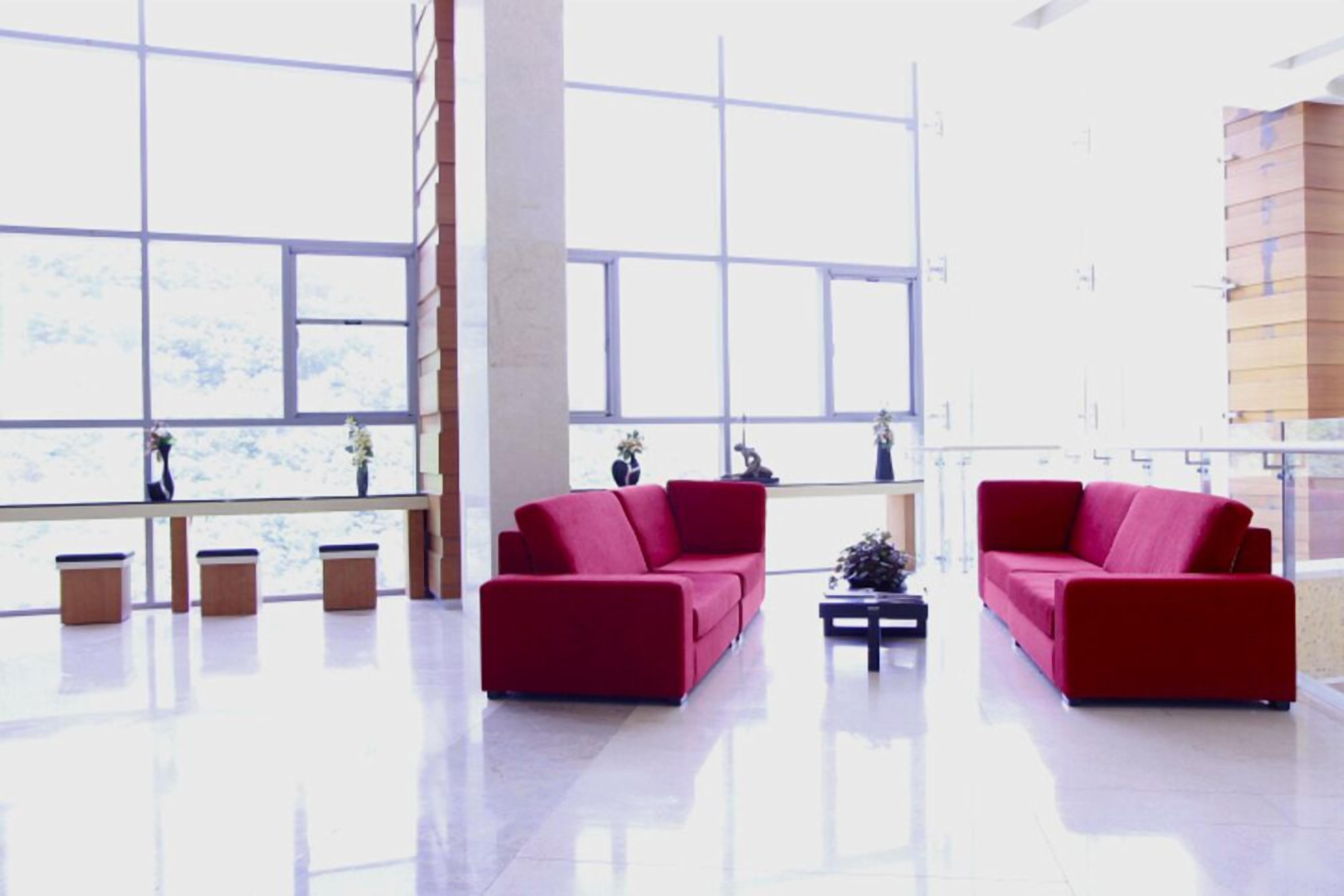 A spacious lobby with large windows, two red sofas, and a coffee table.