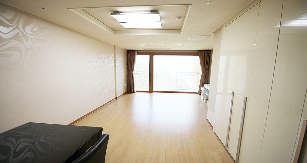 A spacious room with a large sliding glass door leading to a balcony, a ceiling light fixture, and a black table.